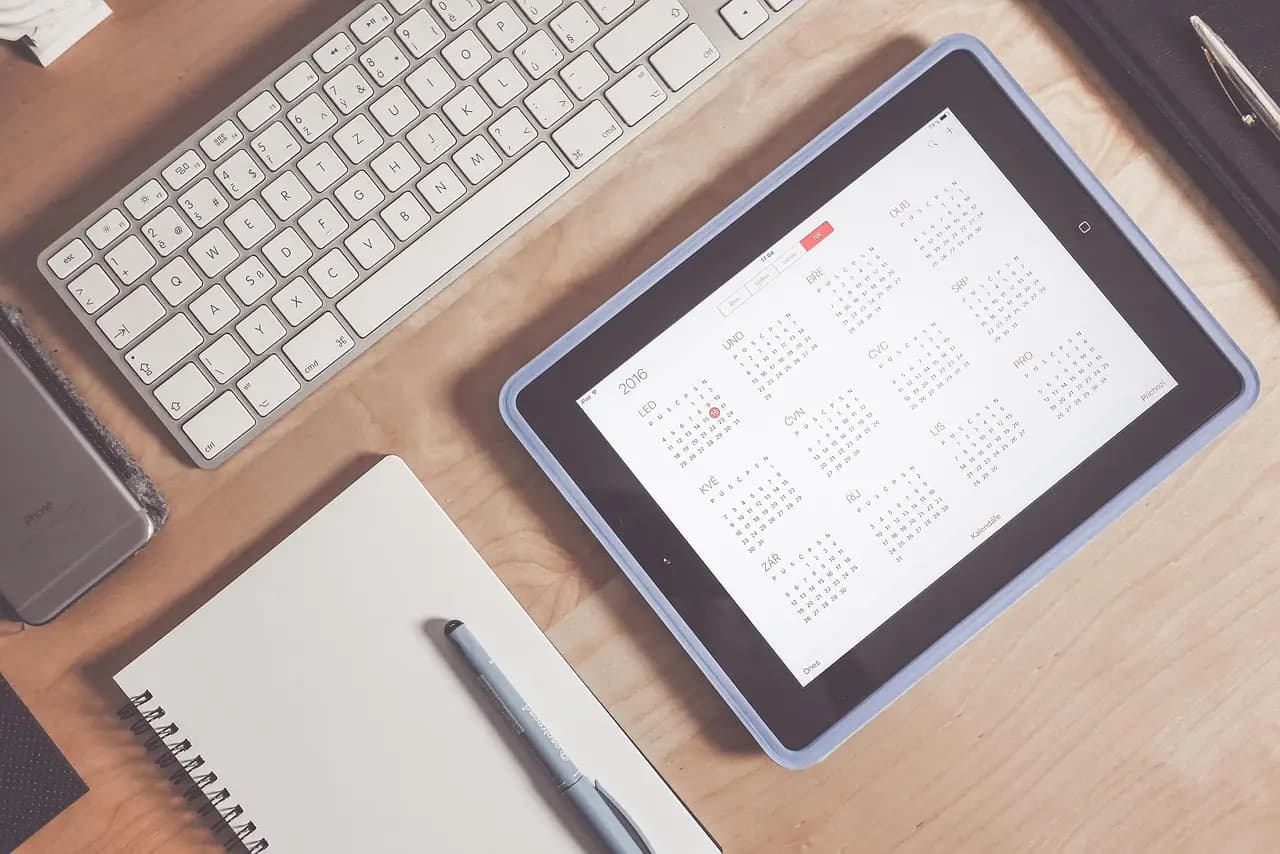 Tablet showing a year calendar alongside a keyboard and notepad, representing 1Social's scheduling and content planning features